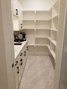 an empty walk in closet with white cabinets and marble flooring on the side wall