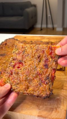 a person holding up a piece of food on top of a wooden cutting board