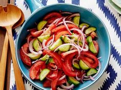 a blue bowl filled with sliced red onions and cucumbers next to wooden spoons