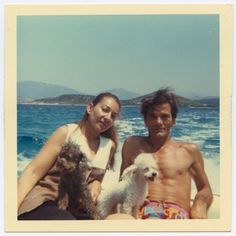 a man and woman sitting on the beach with a dog in front of their backs