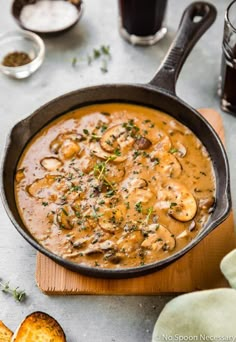 a skillet filled with mushrooms and gravy on top of a wooden cutting board