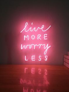 a pink neon sign that says live more worry less on top of a wooden table