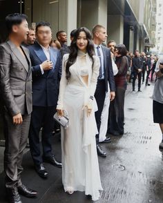 a woman in a white dress standing next to a group of people on a sidewalk