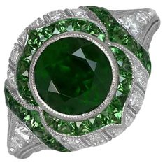 This exquisite gemstone ring showcases a certified 2.07-carat Natural Dementoid Garnet, validated by GRS, and untouched by heat treatment. The central gem is encircled by a halo of French-cut natural Tsavorite garnets. The ring's design is further enhanced by the presence of round brilliant cut diamonds and Tsavorite Garnets. The center stone is securely bezel set in 18k yellow gold, while the ring itself is masterfully hand-crafted in 18k white gold. The center stone is certified by GRS: 2.07-c Garnet Engagement Ring, Tsavorite Garnet, French Cut, Garnet Stone, Stone Cuts, Jewelry Rings Engagement, Round Brilliant Cut Diamond, Gemstone Ring, Round Brilliant