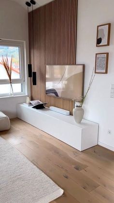 a flat screen tv sitting on top of a white shelf in a living room next to a window