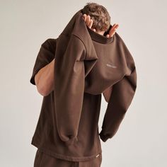 a man wearing a brown sweatshirt and sweatpants is covering his face with his hands