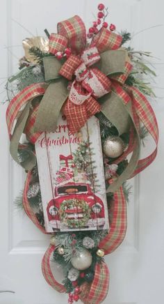 a christmas wreath hanging on the front door with an old truck and evergreens in it