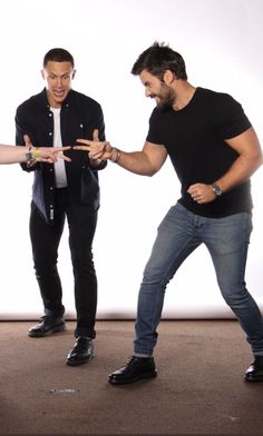 two men standing next to each other in front of a white background with one pointing at another man's hand