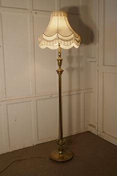 a floor lamp with a white shade on it's base in front of a wall