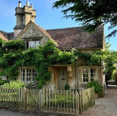 an old stone house with ivy growing on it's roof and fenced in yard