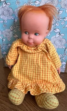 an old doll with red hair wearing a yellow dress sitting on a wooden floor next to a blue and white wall