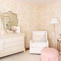 a baby's room with floral wallpaper and white furniture, including a pink ottoman