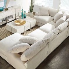 a large white couch sitting in a living room next to a table with two vases on it