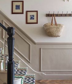 there is a basket hanging on the wall next to some stairs with pictures above it