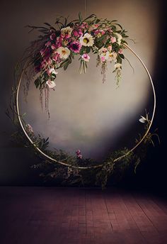 a circle with flowers and greenery hanging from it's sides on a wooden floor