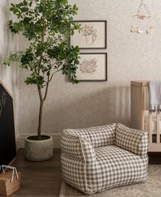 a baby's room with a chair, potted tree and pictures on the wall