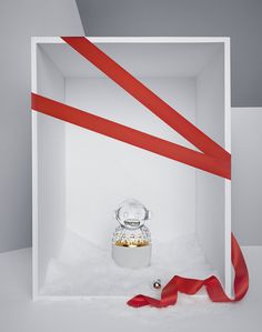 a white box with red ribbon around it and a glass jar in the middle, on top of snow