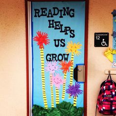 a bulletin board with flowers on it in front of a door that says reading helps us grow