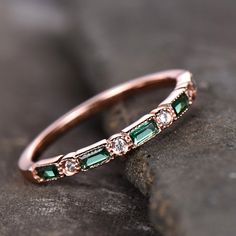 a rose gold band with emeralds and diamonds on it, sitting on a rock