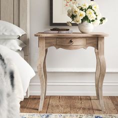 a small table with flowers on it next to a bed and a framed photograph in the background