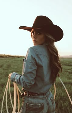 a woman wearing a cowboy hat and holding a lasso in her hand while standing in a field