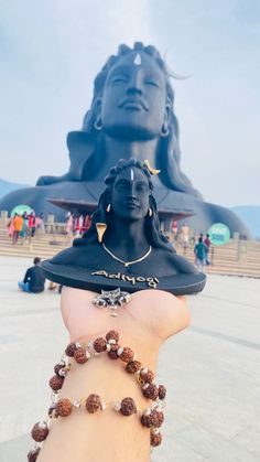 a hand holding a beaded bracelet in front of a large statue with a woman's head on it