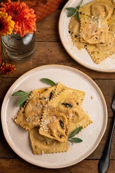 two white plates topped with ravioli on top of a wooden table next to an orange flower