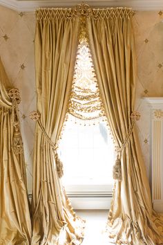 an open window with gold curtains in front of it and a chandelier hanging from the ceiling