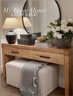 a wooden table topped with a mirror next to a lamp and vase filled with flowers