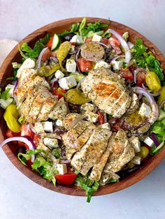 a salad with chicken, tomatoes, onions and feta cheese in a wooden bowl