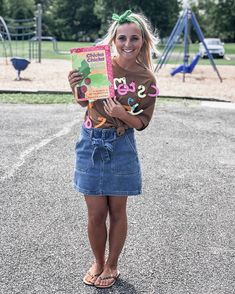 a woman is standing in the parking lot holding a book and smiling at the camera