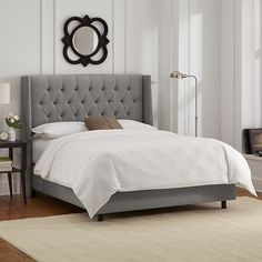 a bed with white sheets and black headboard in a small room next to a mirror