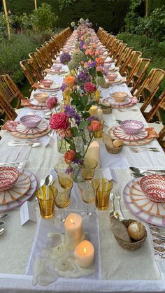 a long table is set with plates and candles for an outdoor dinner party in the garden