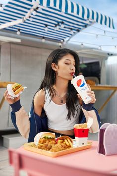 a woman sitting at a table eating food and drinking from a carton with a drink in her hand