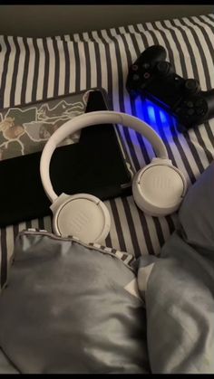 headphones and remotes are laying on a bed with striped sheets in the background