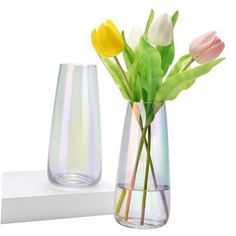 two vases with flowers in them sitting on a shelf next to each other,