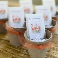 small flower pots with cards in them on a wooden table, decorated with orange ribbon