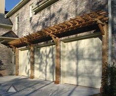 a wooden pergoline attached to the side of a brick building next to a driveway