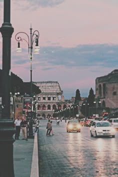 cars are driving down the street in front of an old building at dusk with people walking on the sidewalk