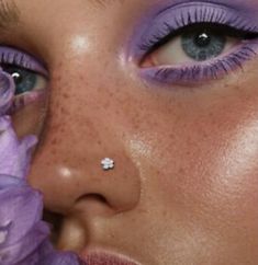 a close up of a woman's face with purple makeup and flowers in front of her