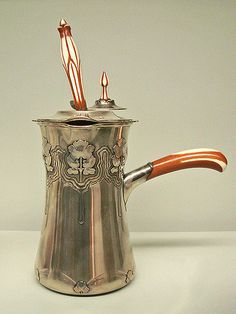 a silver tea pot with two wooden spoons sticking out of it's top