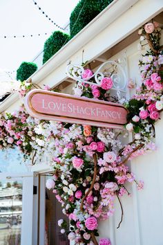 a sign that says love shackancy hanging from the side of a building with flowers on it