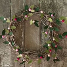 a wreath with pink and green leaves hanging on a wooden wall