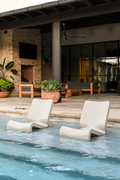 two lawn chairs sitting on the edge of a pool in front of a house with an open patio