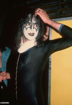 a man with his face painted in black and white is standing next to a yellow wall