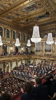 an orchestra performing in a large building with chandeliers hanging from the ceiling and people sitting