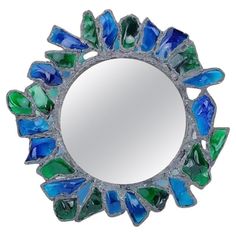 a round mirror with green, blue and white glass pieces on the bottom of it