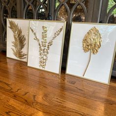 three framed art pieces sitting on top of a wooden table