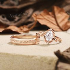 two gold wedding rings with leaves on the ground next to each other and one has a white diamond in it