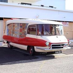 an old red and white bus parked in front of a building with a sign on it's side